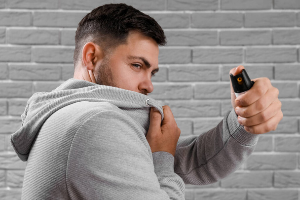Young man with pepper spray for self-defence on grey brick background, closeup - Fotografie, Obrázek
