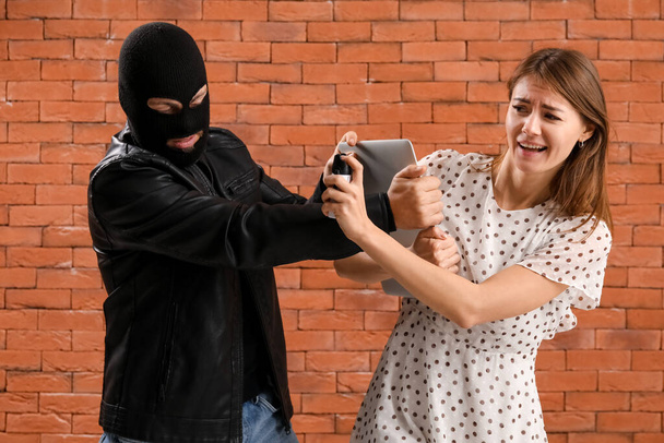Young woman with pepper spray defending herself against thief on brick background - Foto, imagen