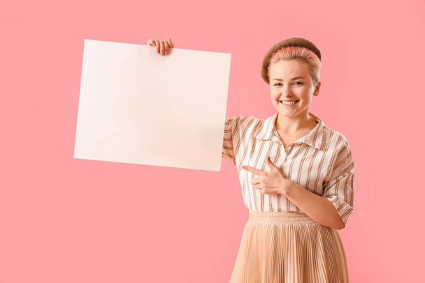Young woman pointing at blank poster on pink background - 写真・画像