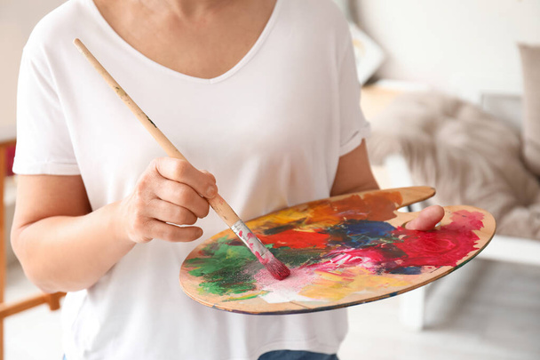 Mature female artist with palette and brush in  workshop, closeup - Fotó, kép