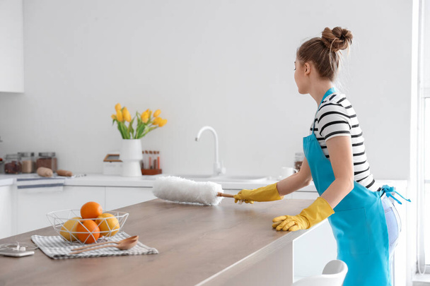 Mujer bastante joven limpiando mesa de comedor con cepillo de polvo en cocina ligera - Foto, Imagen