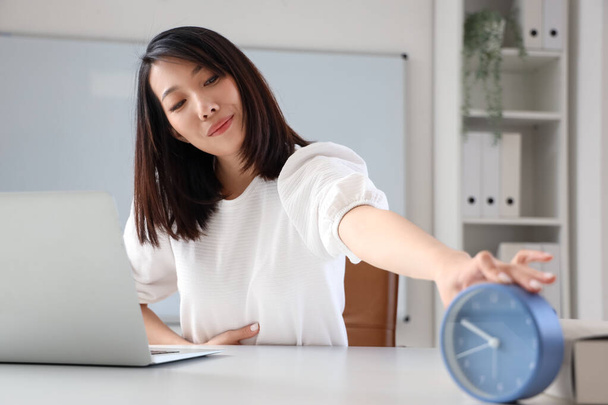 Asian woman taking alarm clock in office - Foto, afbeelding