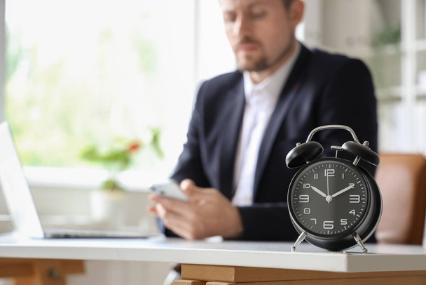 Alarm clock on table of businessman in office, closeup - Foto, afbeelding