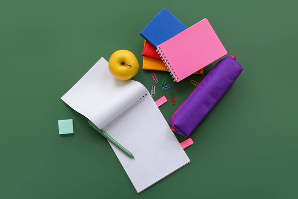 Σημειωματάρια με φρέσκο μήλο και διάφορα χαρτικά σε πράσινο φόντο - Φωτογραφία, εικόνα