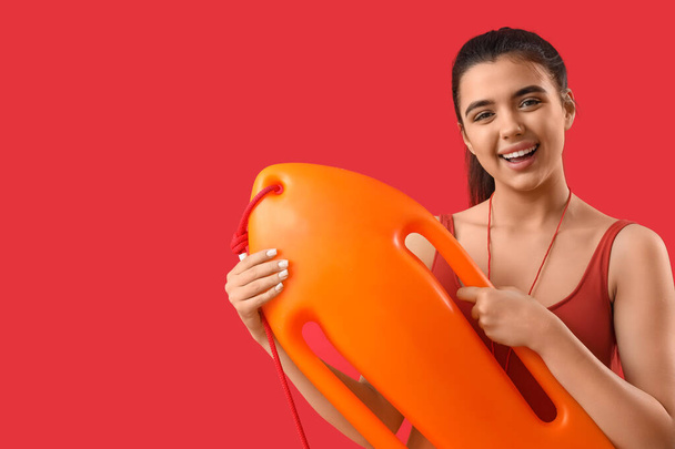 Female lifeguard with rescue buoy on red background - Fotoğraf, Görsel