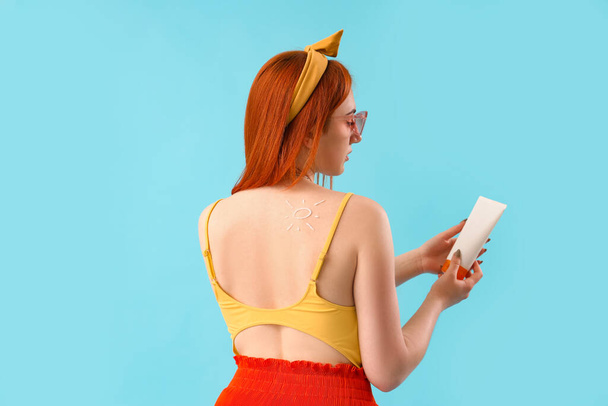 Jonge vrouw met zon gemaakt van zonnebrandcrème op blauwe achtergrond, achteraanzicht - Foto, afbeelding