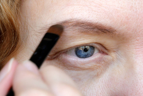 vrouwelijk oog van middelbare leeftijd met hangend ooglid dat make-up doet. Ptosis is een hangende van het bovenste ooglid, lui oog. Cosmetologie en gezichtsconcept, eerste rimpels, close-up - Foto, afbeelding