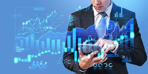 Unrecognizable businessman using tablet computer over blue background with double exposure of digital financial diagrams. Concept of stock market and investment apps - Foto, Imagem
