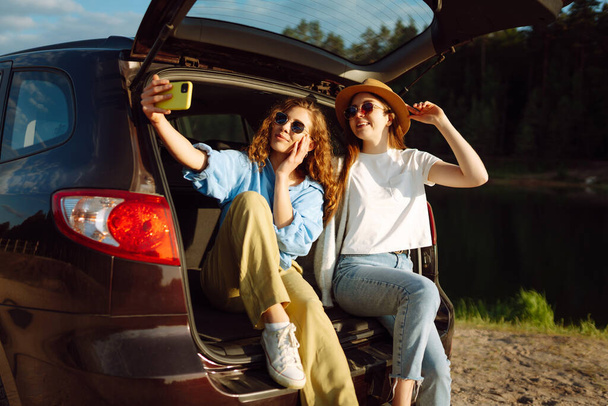 Two Young woman takes a selfie in the car during a road trip. Lifestyle, travel, tourism, nature, active life. - Fotografie, Obrázek