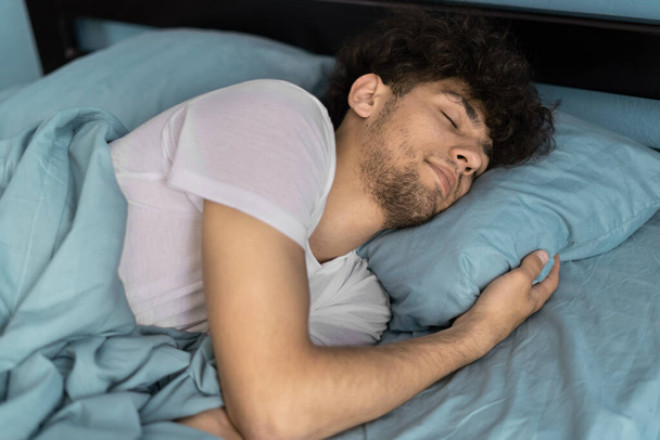 Widok na młodego człowieka śpiącego dobrze w poduszce do przytulania. Facet lubi pościel i materac w sypialni. Dobry pomysł na sen.. - Zdjęcie, obraz