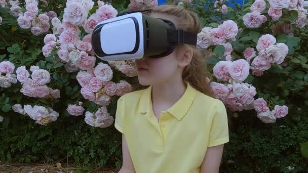 La chica lleva un casco de realidad virtual en la cabeza. Una chica juega en gafas de realidad virtual en la calle. - Imágenes, Vídeo