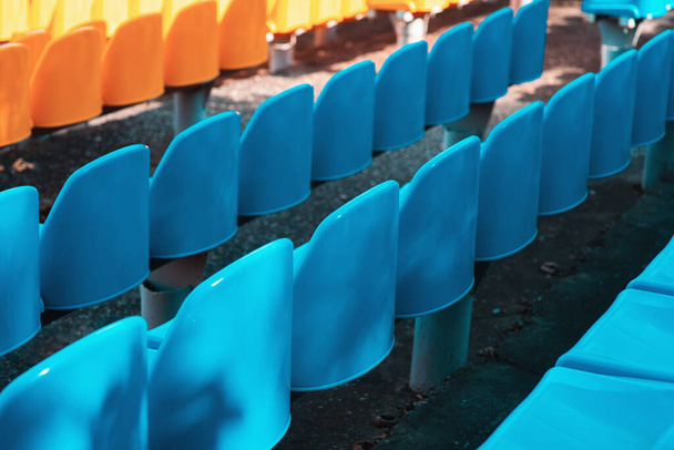 Hay filas vacías de asientos en el estadio. Sillas azules y amarillas, nadie presente en un espectáculo deportivo concepto abstracto simple. Silla filas de cerca, vista lateral - Foto, imagen
