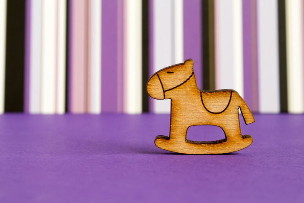 Wooden icon of children's rocking horse on purple striped backgr - 写真・画像