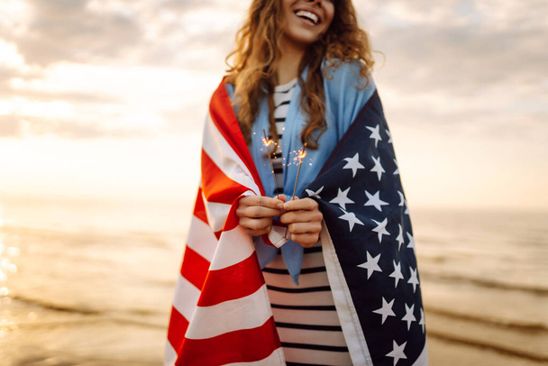 Young woman with American flag  and sparklers on the beach. Patriotic holiday. USA celebrate 4th of July. Independence Day concept - Foto, afbeelding