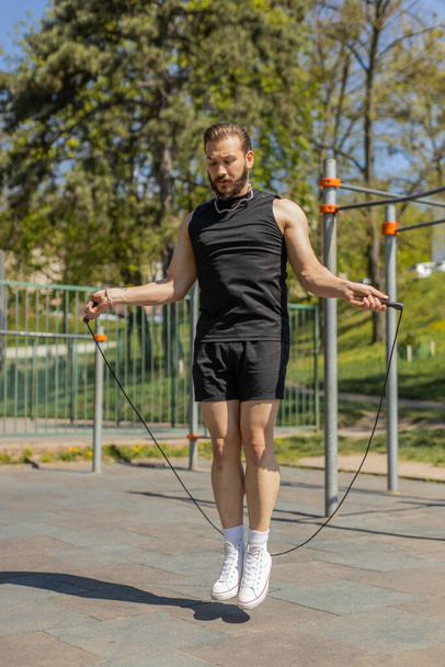 Athletic lebanese man in sportswear skipping rope. Young middle eastern arabian guy doing jumping exercises on playground. Sports crossfit, fitness routine, workout. Strength motivation. Outdoors - Photo, Image