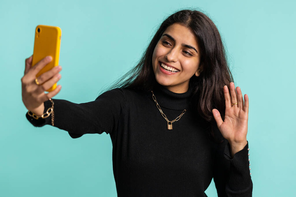 Indyjska kobieta podróżnik blogger, robienie selfie na smartfonie, komunikowanie rozmowy wideo online z rodziną lub przyjaciółmi, Transmisja na żywo. Pretty Hinduska dziewczyna odizolowany na niebieskim tle, wewnątrz - Zdjęcie, obraz