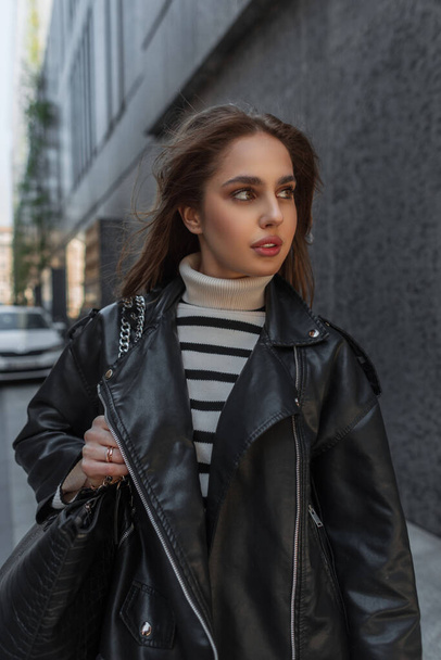Urban fashion beautiful woman in stylish rock casual clothes with black leather jacket and bag walks in the city - Fotografie, Obrázek