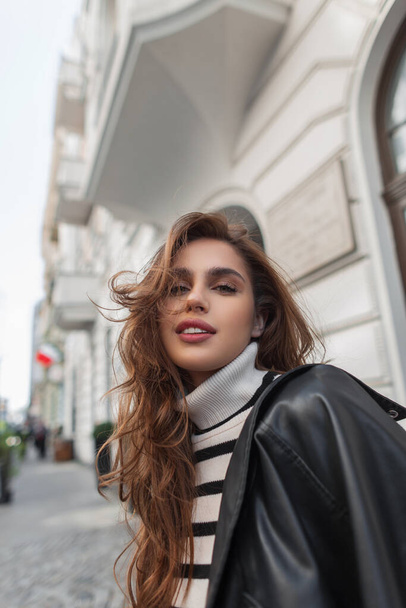 Moda joven hermosa chica modelo con suéter de moda con chaqueta de cuero negro camina en la ciudad - Foto, imagen