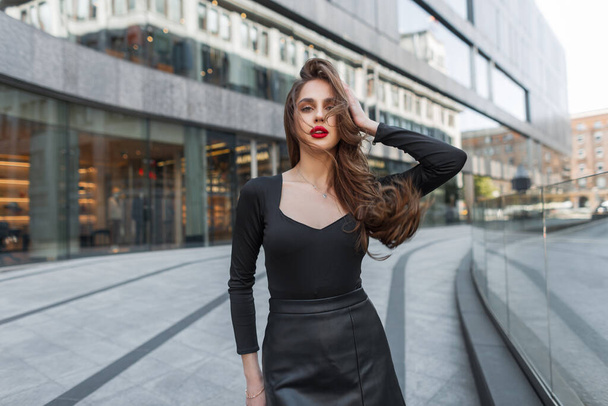 Fashionable beautiful young woman model with red lips in fashion black clothes walks and poses in the city - Фото, зображення