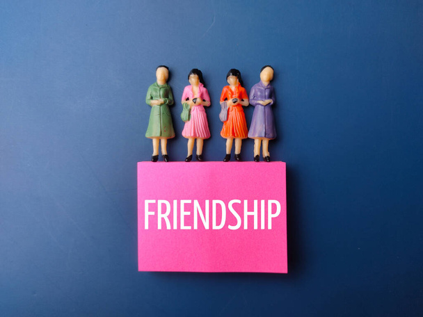 Miniatuur mensen en gekleurde noot met het woord FRIENDSHIP op blauwe achtergrond - Foto, afbeelding