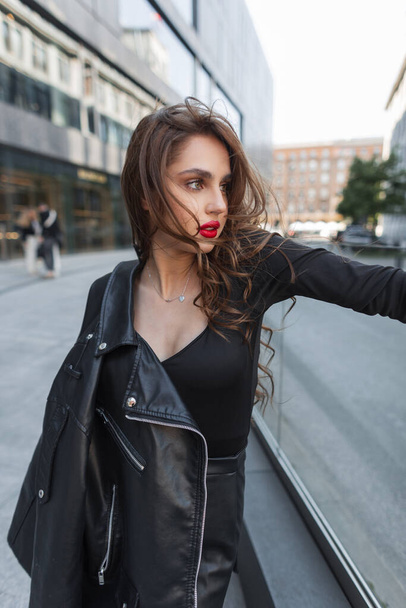 Eleganz modische junge schöne schicke Frau mit roten Lippen in schwarzer Modekleidung mit Lederjacke spaziert durch die Stadt - Foto, Bild