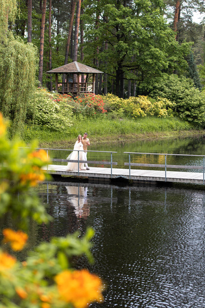 Romantische Schwangere spazieren auf Holzbrücke in grün blühender Natur - Foto, Bild