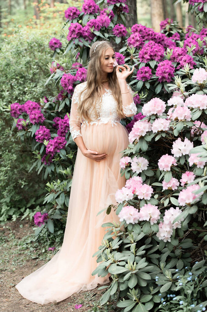 Schwangere steht im Rhododendronpark. Großaufnahme von Schwangerschaftsbauch in blühender Natur. - Foto, Bild
