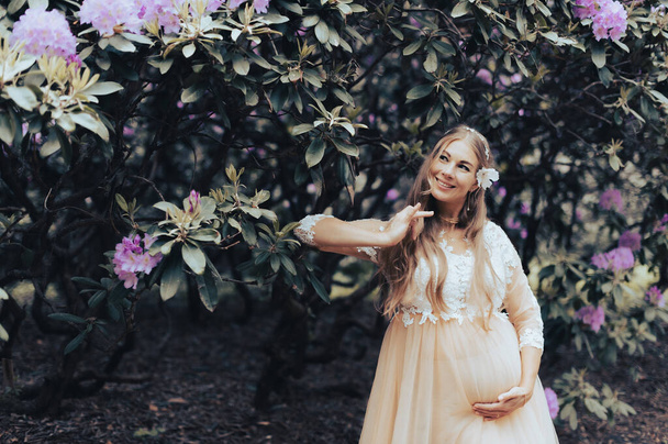 Romantikus terhes nő visel luxus ruha tánc egy virágzó rododendron park - Fotó, kép