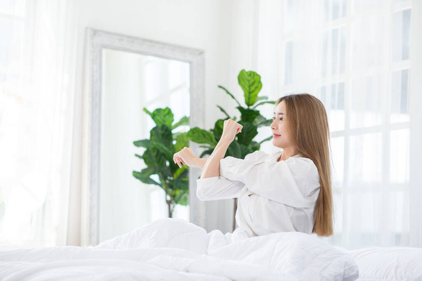 Beautiful Asian young Woman stretching her arm after wake up on bed and looking outside windows in cozy bedroom feeling so fresh and relax in the morning.Health care Concept  - Фото, изображение
