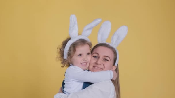 Attractive young woman with little cute girl in bunny ears kissing, hugging isolated on yellow background. Vertical video - Footage, Video