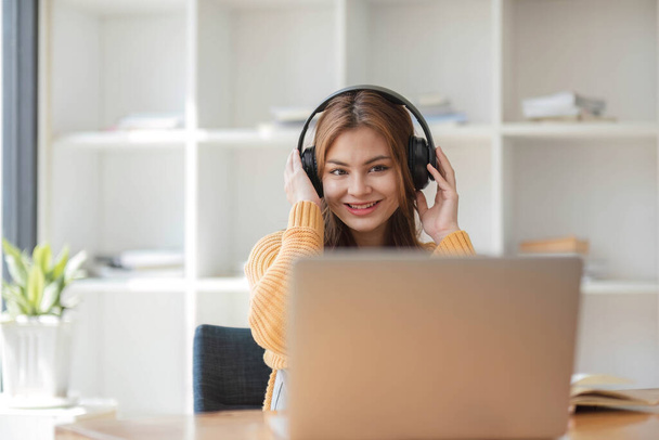 Kulaklıklı Asyalı bir kadın internetten ders çalışmaya ara verip iş sırasında müzik dinlemekten mutlu bir şekilde müzik dinliyor. - Fotoğraf, Görsel
