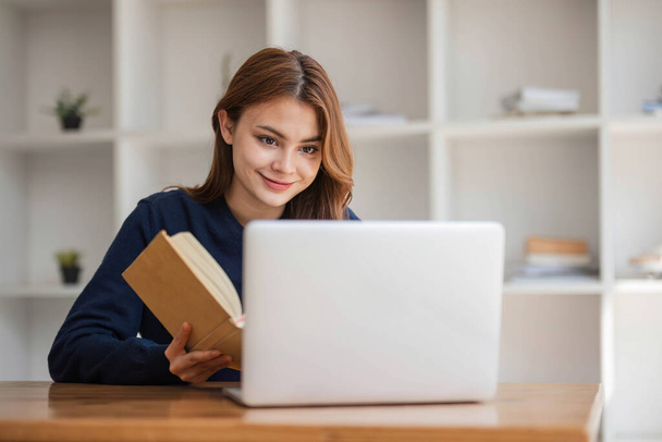 アジアの学部生の10代の女の子は、ノートパソコンの本と図書館で勉強しますオンライン学習のための研究を行います,エッセイ宿題の割り当てのためのメモを作ります,オンライン教育eラーニングの概念 - 写真・画像