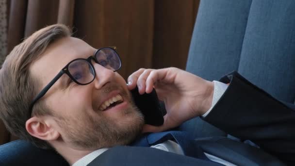 Χαρούμενος επιχειρηματίας μιλάει στο τηλέφωνο κατά τη διάρκεια ενός διαλείμματος. Κλείσε. Επιχειρηματίας χαλαρώνοντας στον καναπέ στο γραφείο ως επιχειρηματική ιδέα. - Πλάνα, βίντεο