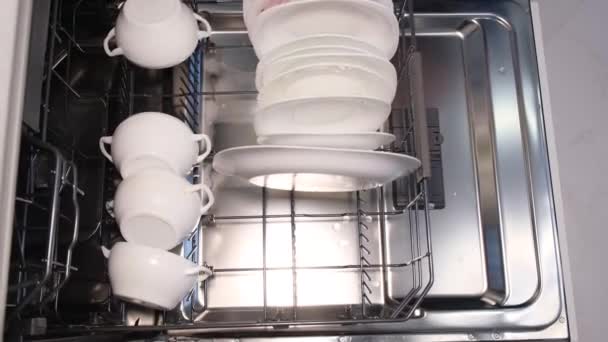 Bir kadın lastik eldiven verip, beyaz tabak ve bardakları bulaşık makinesine koyar. İleri teknolojileri kullanarak yüksek kaliteli mutfak gereçleri. - Video, Çekim