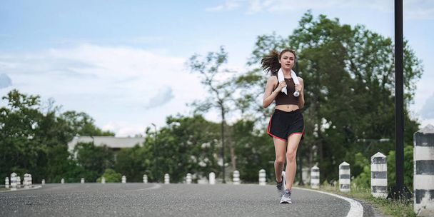 若い魅力的な美しいアスレチックランナーの女性は緑の公園ジョギングで実行されます。健康で活動的なライフスタイルのコンセプト. - 写真・画像