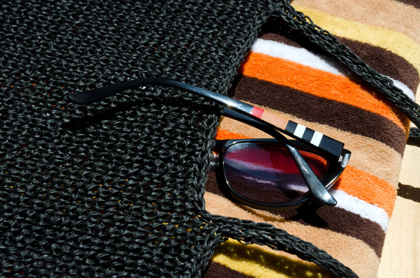 Fekete raffia strandtáska. Női táska törölközővel és napszemüveggel az asztalon. - Fotó, kép