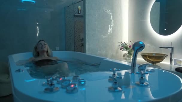 Tyytyväinen nuori nainen, jolla on suljetut silmät rentouttava vesihieronnan aikana kylpylässä. Vesihierontamenetelmistä saatava nautinto - Materiaali, video
