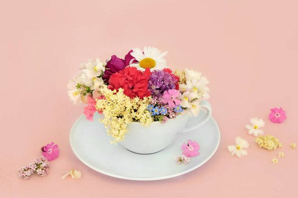Surrealistische zomerbloem en wilde bloem theekopje compositie op roze achtergrond met verspreide bloemen. Abstract plezier gezondheid voedsel bloemen natuur surrealisme ontwerp. - Foto, afbeelding
