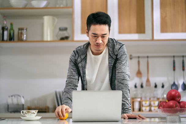 joven asiático hombre de negocios trabajando en cocina en casa usando laptop ordenador - Foto, imagen