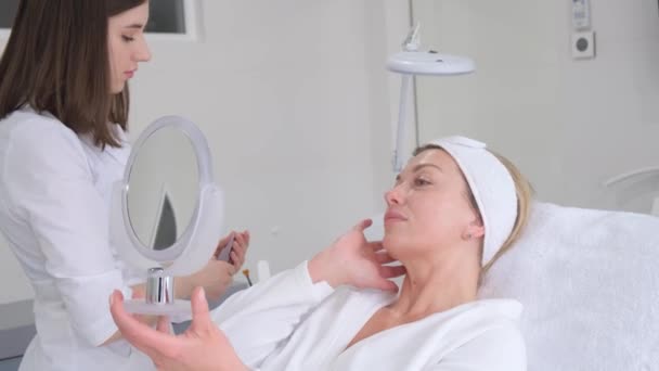 Een schoonheidsspecialiste brengt een masker aan op een vrouwengezicht in een schoonheidssalon en communiceert met haar. Hoge kwaliteit 4k video - Video
