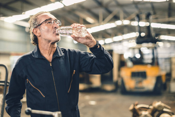 Durstige ältere männliche Mitarbeiter trinken Wasser erfrischend von müder harter Arbeit am heißen Arbeitsplatz - Foto, Bild