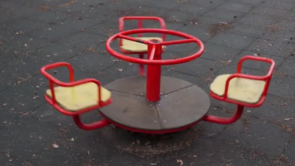 Een lege rode kinderdraaimolen draait in een stadspark na regen van dichtbij. Eenzame schommel draait op de speelplaats in de tuin. Oude verlaten speelveld zonder kinderen. Videobeelden in 4k 25FPS - Video
