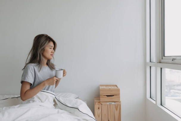 Asian woman drinking coffee right after wake up on the bed in the morning. - Photo, Image