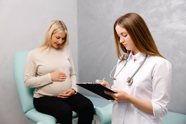 Gynecologist talking with a young female patient during a medical consultation in the gynecological office and and making entries in the patient's medical record. - Foto, Imagem
