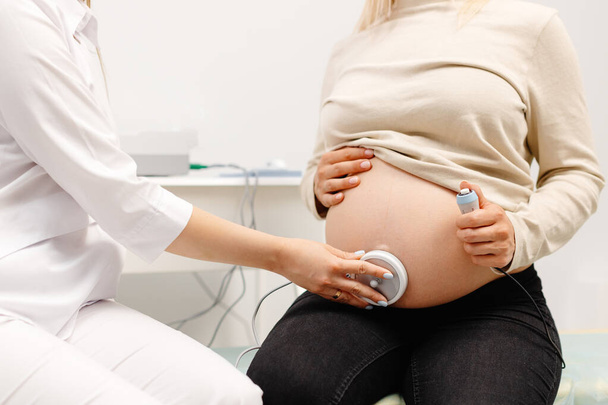 Lääkäri valmistelee raskaana olevan naisen sikiön sykkeen tarkistamiseen sikiön seurannan avulla - Valokuva, kuva