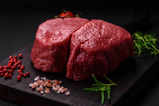 Raw beef eye steak round with salt, spices and herbs prepared for grilling on a textured background - Photo, Image
