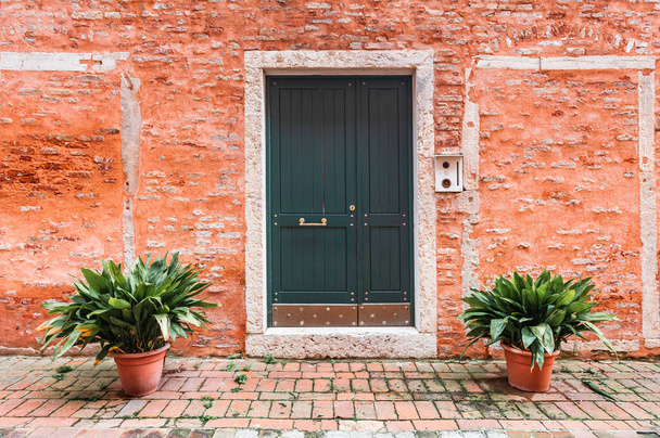 Red brick facade of the house with wooden door and flowers. Old medieval architecture in Venice, Italy. - Foto, Bild
