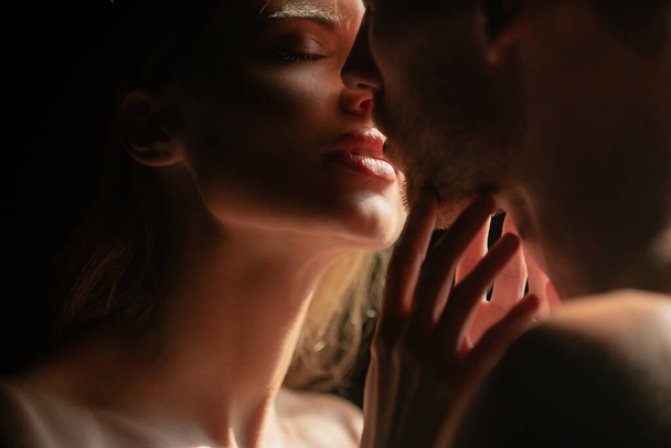 Close up face of sensual portrait of a sexy couple embracing while dating. Young couple in love on black. The lovely coupl spends time together. Sensual couple in the tender passion - 写真・画像
