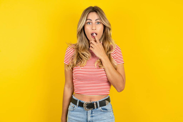 Zenuwachtig verbaasd Jonge mooie vrouw draagt gestreepte t-shirt over gele achtergrond opent mond van verrassing, reageert op plotseling nieuws. - Foto, afbeelding