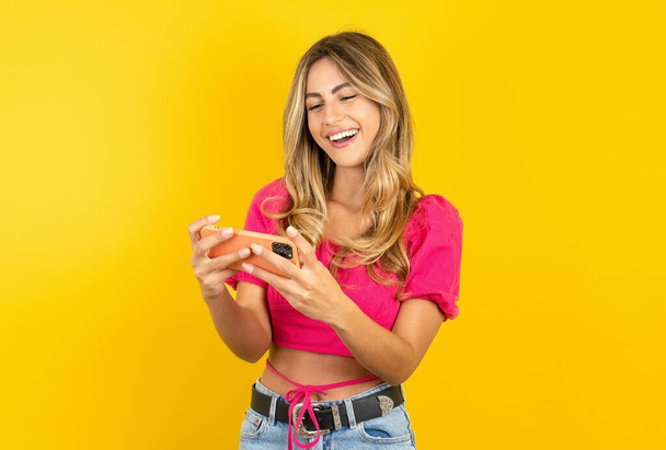 Sarı atölyenin arka planında pembe kırbaç giyen genç ve güzel sarışın bir kadın el ele tutuşup video oyunları oynuyor ya da sohbet ediyor. - Fotoğraf, Görsel